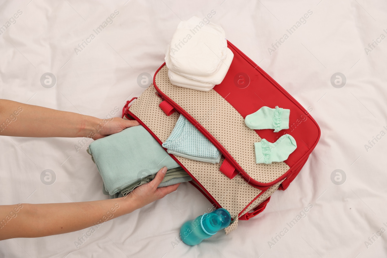 Photo of Mother packing baby's stuff into bag on bed, above view