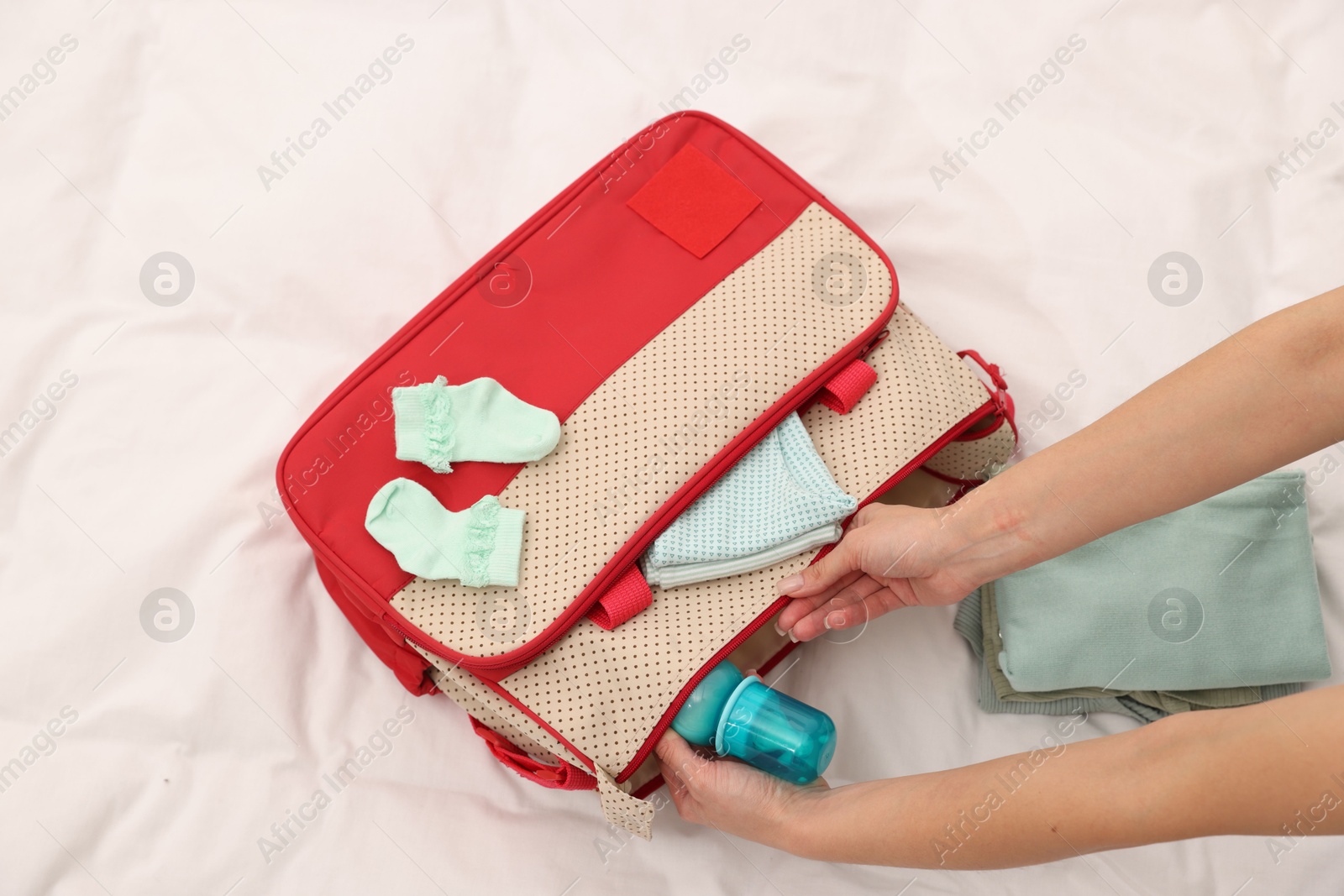 Photo of Mother packing baby's stuff into bag on bed, above view