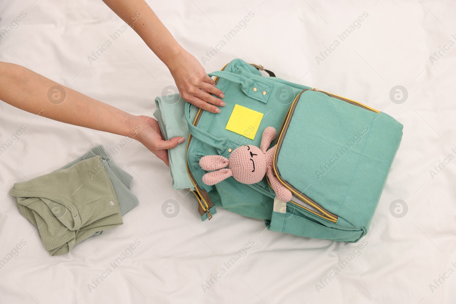 Photo of Mother packing baby's stuff into bag on bed, above view