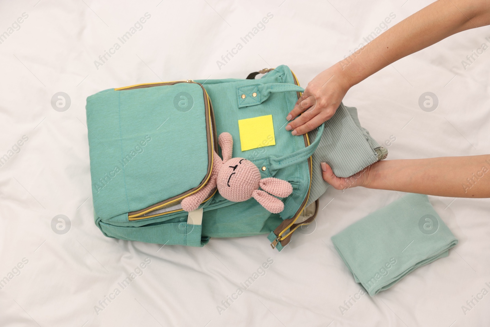 Photo of Mother packing baby's stuff into bag on bed, above view