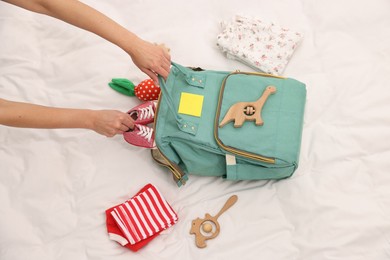 Photo of Mother packing baby's stuff into bag on bed, above view