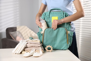 Photo of Mother packing baby's stuff into bag at white table, closeup