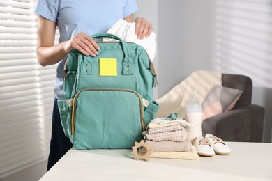 Photo of Mother packing baby's stuff into bag at white table, closeup