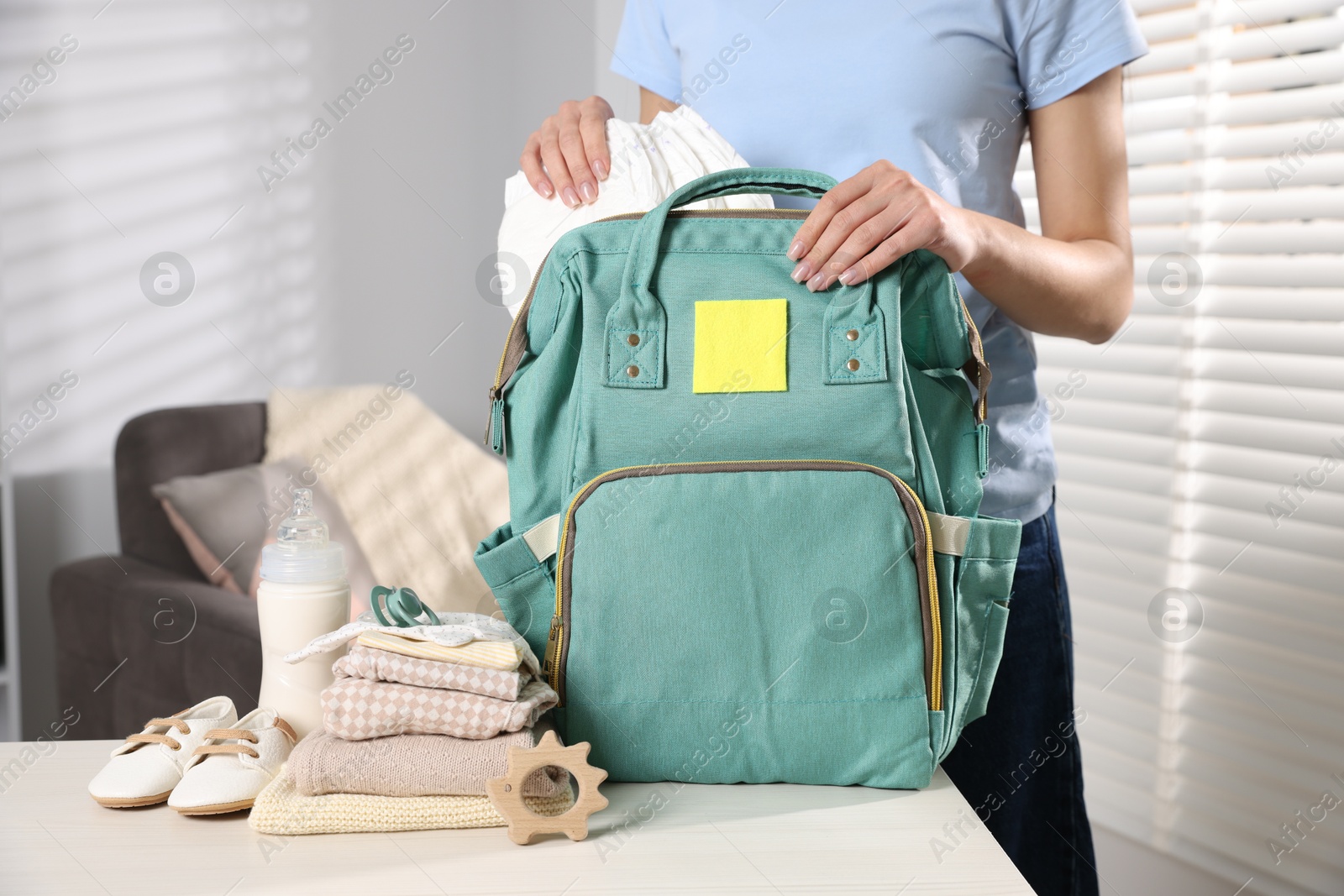 Photo of Mother packing baby's stuff into bag at white table, closeup