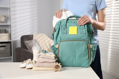 Photo of Mother packing baby's stuff into bag at white table, closeup