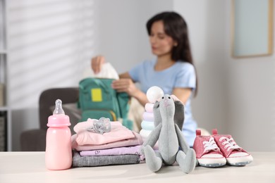 Photo of Baby's stuff on white table and mother packing bag, selective focus