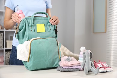 Photo of Mother packing baby's stuff into bag at white table, closeup