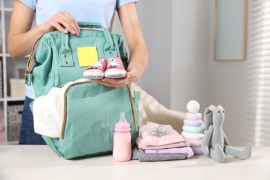 Photo of Mother packing baby's stuff into bag at white table, closeup