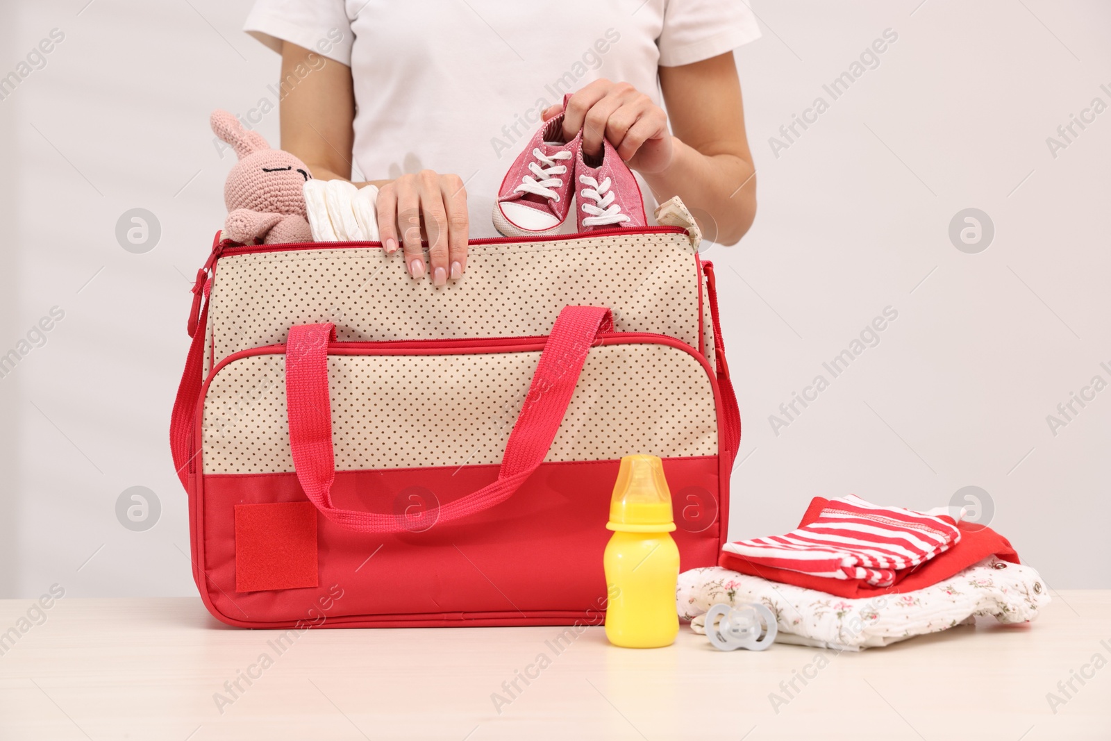 Photo of Mother packing baby's stuff into bag at white table, closeup