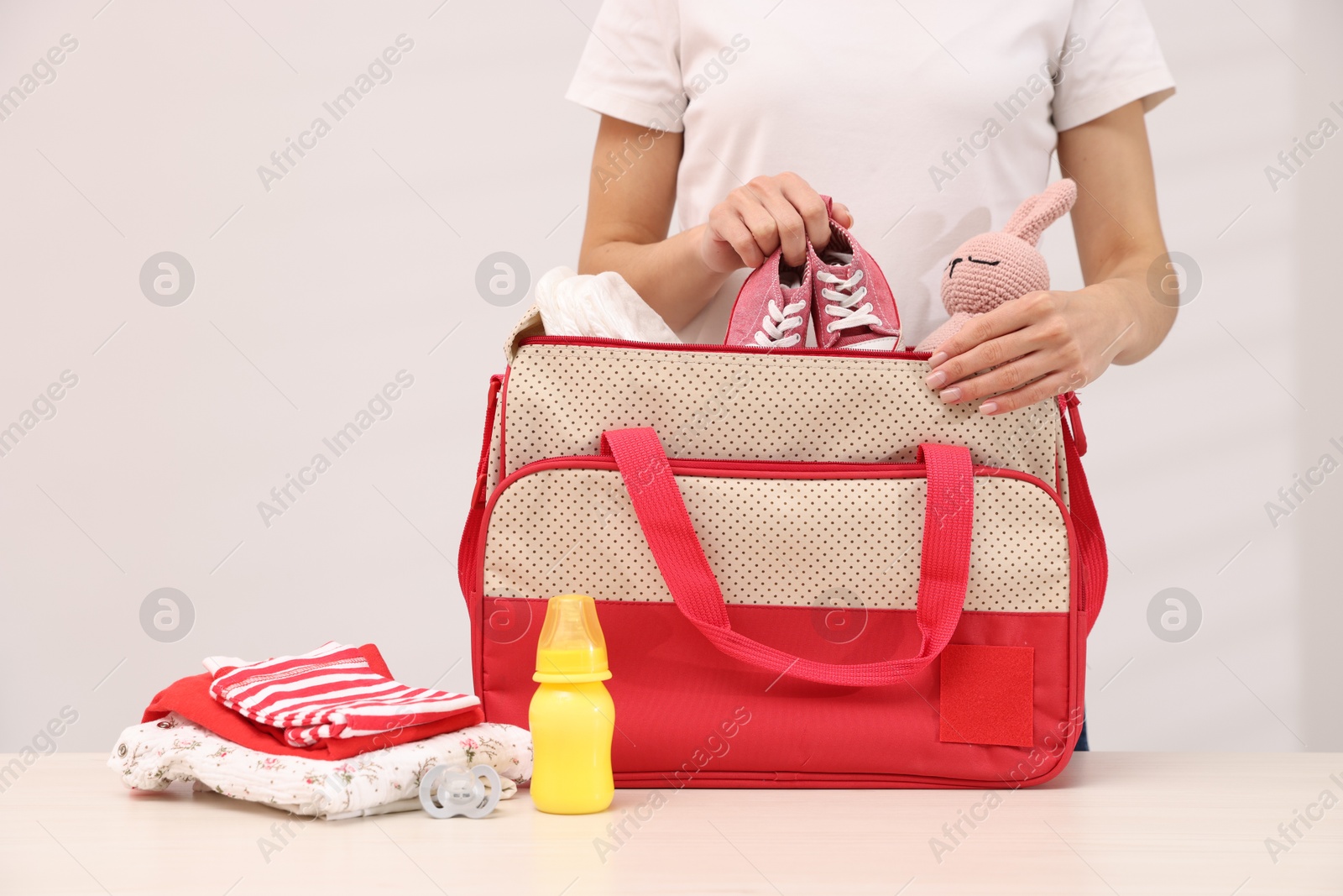 Photo of Mother packing baby's stuff into bag at white table, closeup