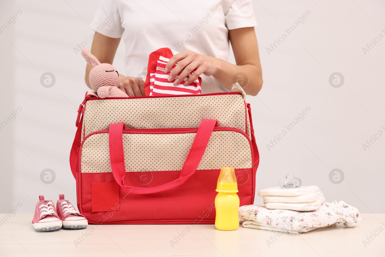 Photo of Mother packing baby's stuff into bag at white table, closeup