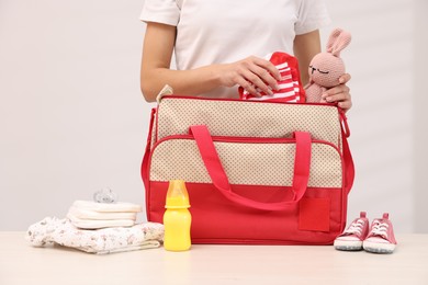 Photo of Mother packing baby's stuff into bag at white table, closeup