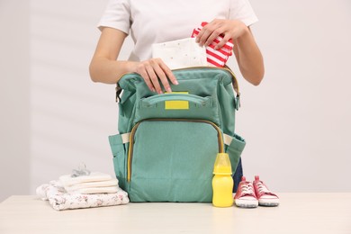 Photo of Mother packing baby's stuff into bag at white table, closeup