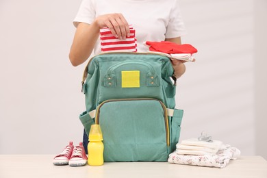 Photo of Mother packing baby's stuff into bag at white table, closeup