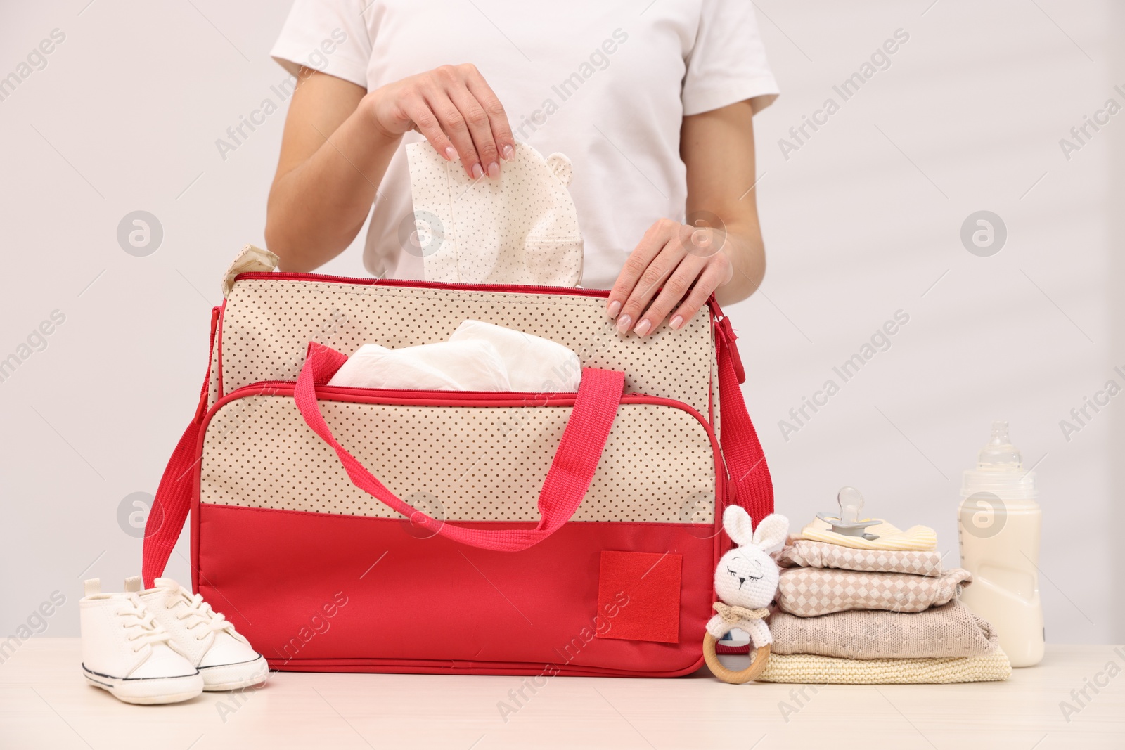 Photo of Mother packing baby's stuff into bag at white table, closeup