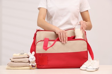 Photo of Mother packing baby's stuff into bag at white table, closeup