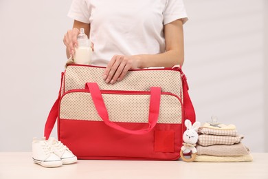 Photo of Mother packing baby's stuff into bag at white table, closeup