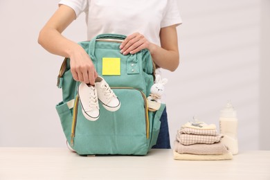 Photo of Mother packing baby's stuff into bag at white table, closeup