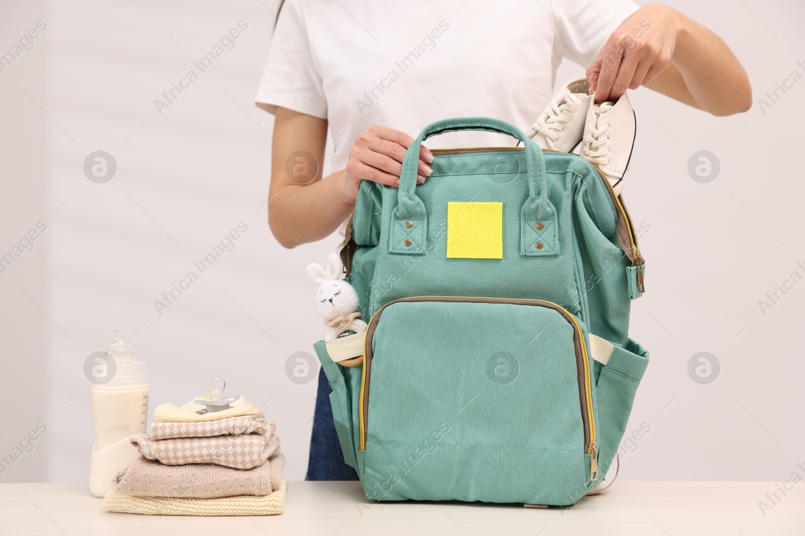 Photo of Mother packing baby's stuff into bag at white table, closeup