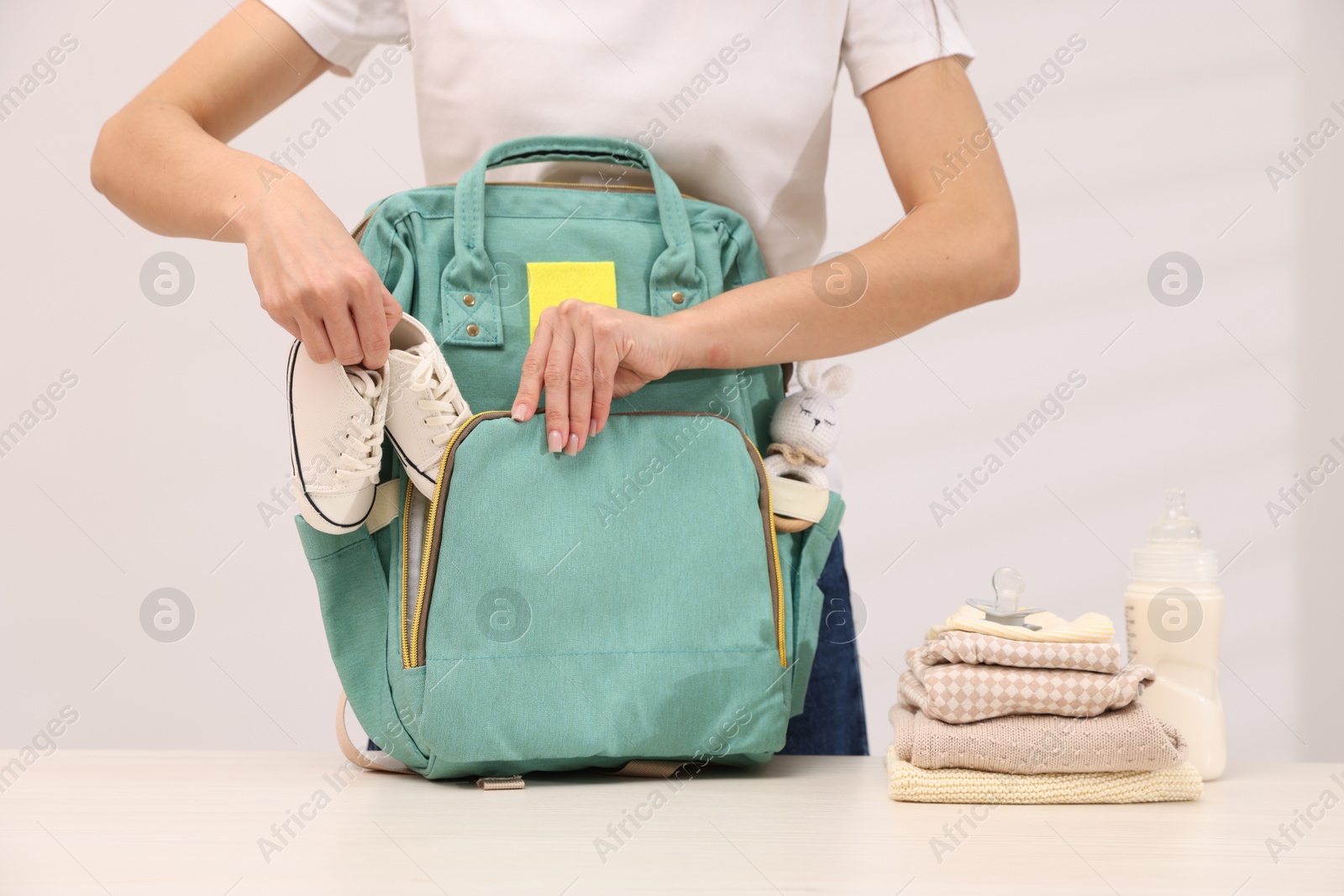 Photo of Mother packing baby's stuff into bag at white table, closeup