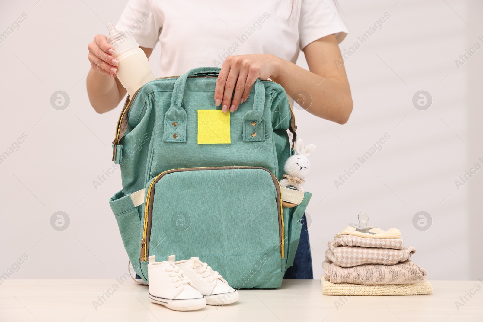 Photo of Mother packing baby's stuff into bag at white table, closeup