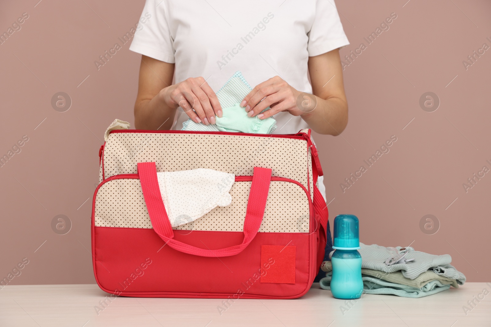 Photo of Mother packing baby's stuff into bag at white table, closeup