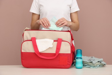 Photo of Mother packing baby's stuff into bag at white table, closeup