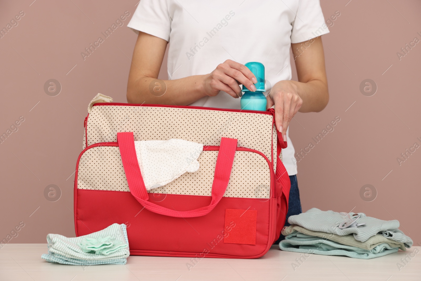 Photo of Mother packing baby's stuff into bag at white table, closeup