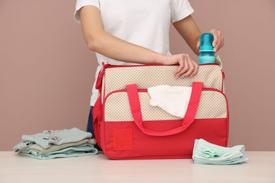 Photo of Mother packing baby's stuff into bag at white table, closeup