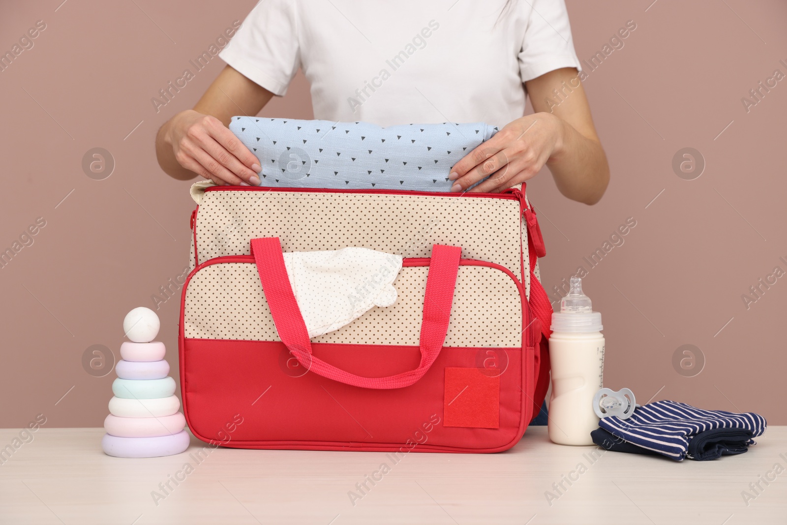 Photo of Mother packing baby's stuff into bag at white table, closeup