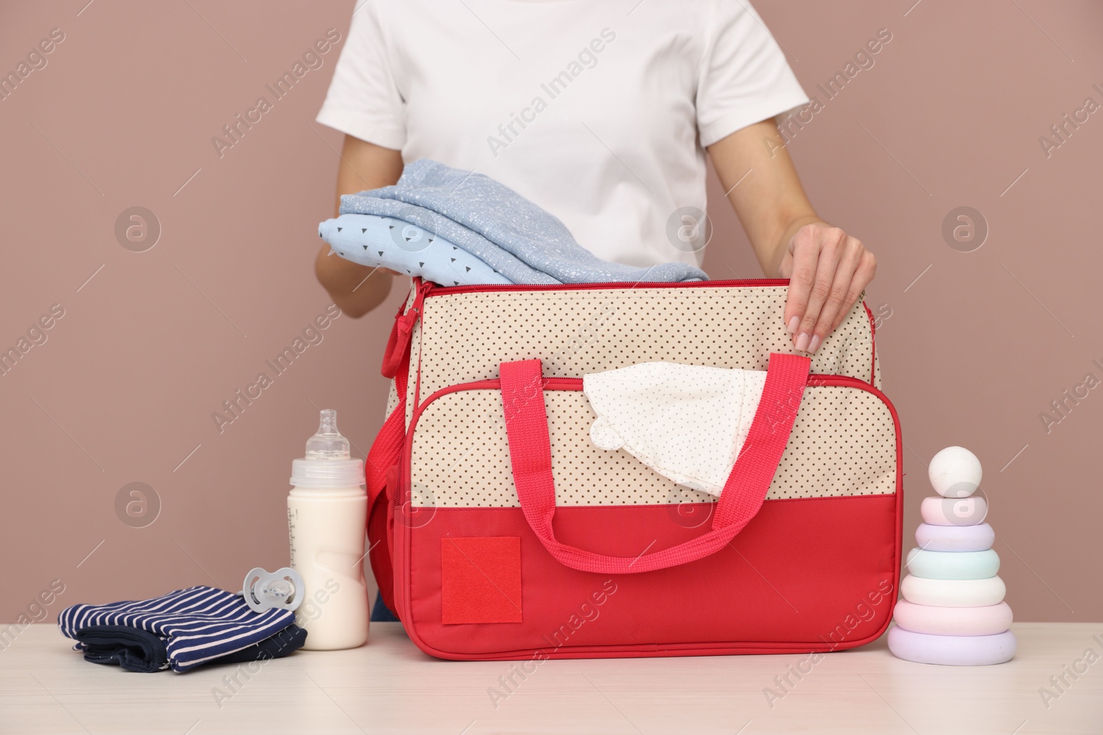 Photo of Mother packing baby's stuff into bag at white table, closeup