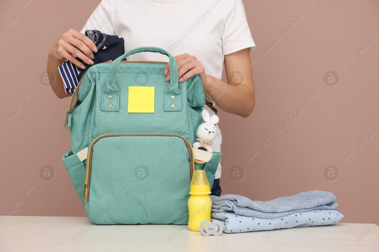 Photo of Mother packing baby's stuff into bag at white table, closeup