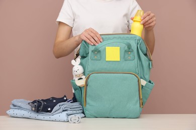 Photo of Mother packing baby's stuff into bag at white table, closeup