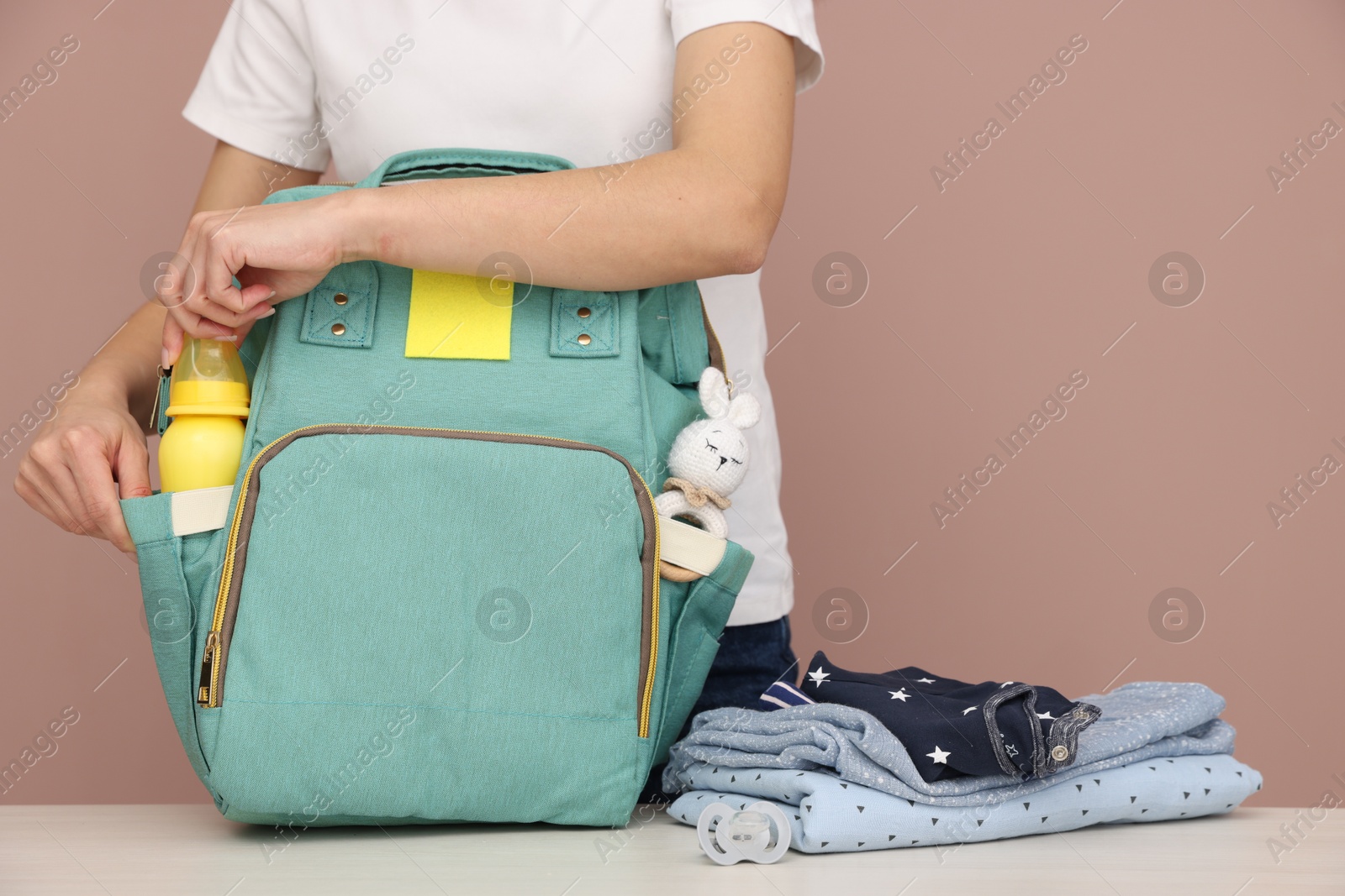 Photo of Mother packing baby's stuff into bag at white table, closeup