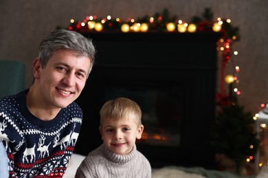 Photo of Dad and son near decorated fireplace at home, space for text. Christmas season