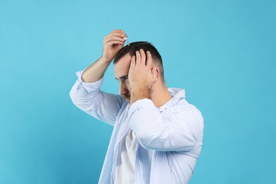 Photo of Baldness treatment. Man applying serum onto hair on light blue background