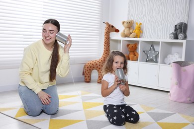 Photo of Woman and girl talking on tin can telephone indoors