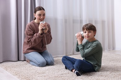 Photo of Woman and boy talking on tin can telephone indoors