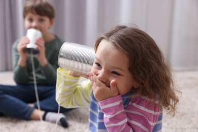 Photo of Boy and girl talking on tin can telephone indoors, selective focus