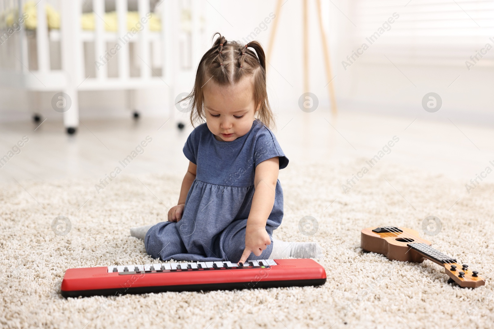 Photo of Cute little girl playing with toy piano at home