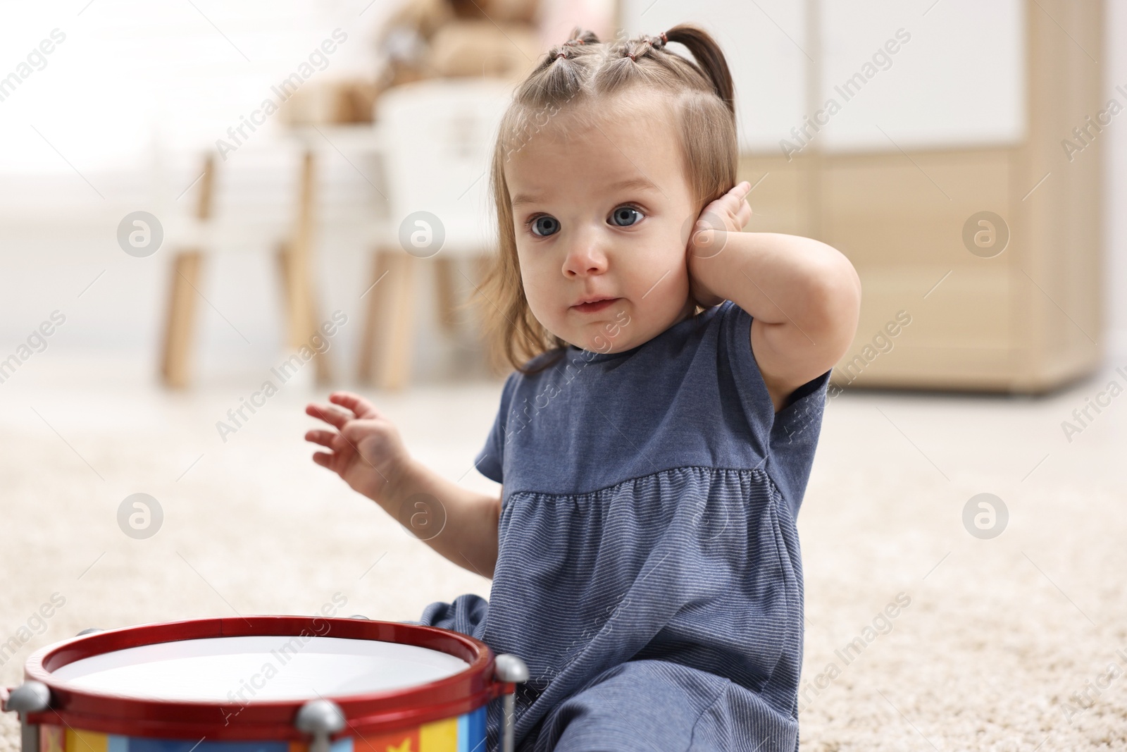 Photo of Cute little girl playing with toy drum on floor at home