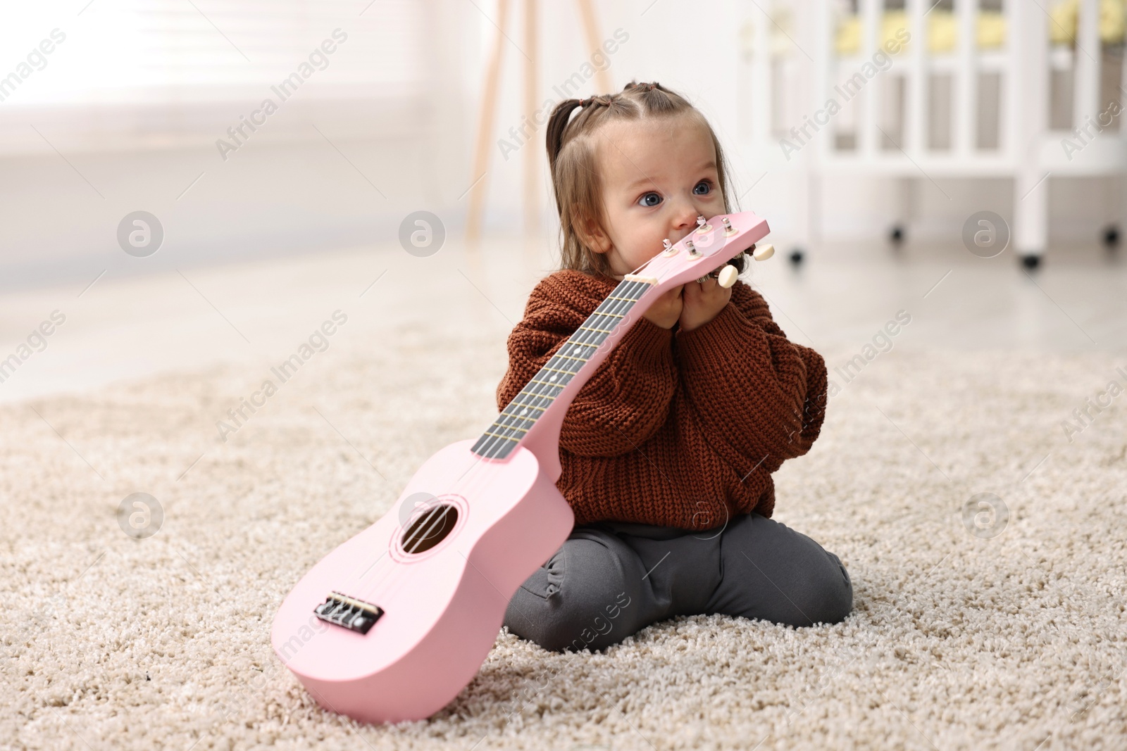 Photo of Cute little girl playing with toy guitar on floor at home