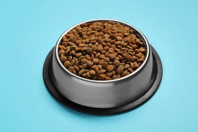 Photo of Dry pet food granules in feeding bowl on light blue background