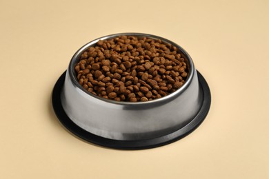 Photo of Dry pet food granules in feeding bowl on pale yellow background