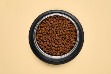 Photo of Dry pet food granules in feeding bowl on pale yellow background, top view