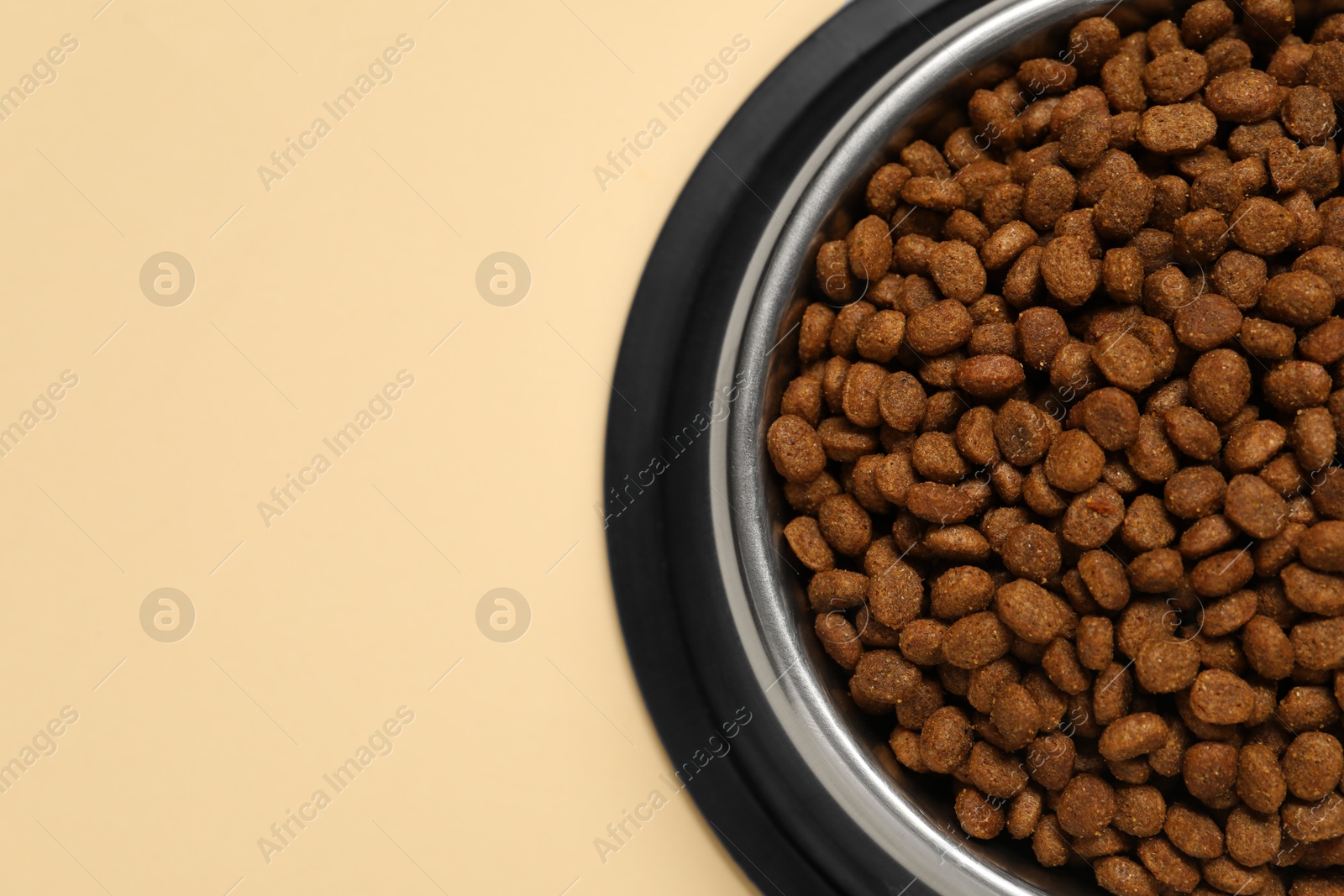 Photo of Dry pet food granules in feeding bowl on pale yellow background, top view. Space for text