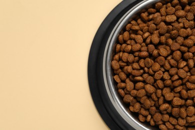 Photo of Dry pet food granules in feeding bowl on pale yellow background, top view. Space for text