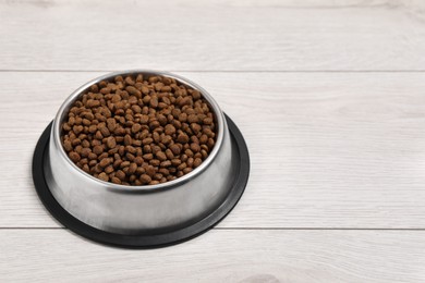 Photo of Dry pet food granules in feeding bowl on floor, space for text