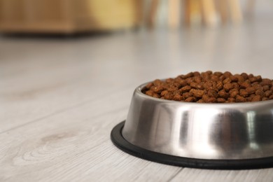 Photo of Dry pet food granules in feeding bowl on floor indoors, space for text