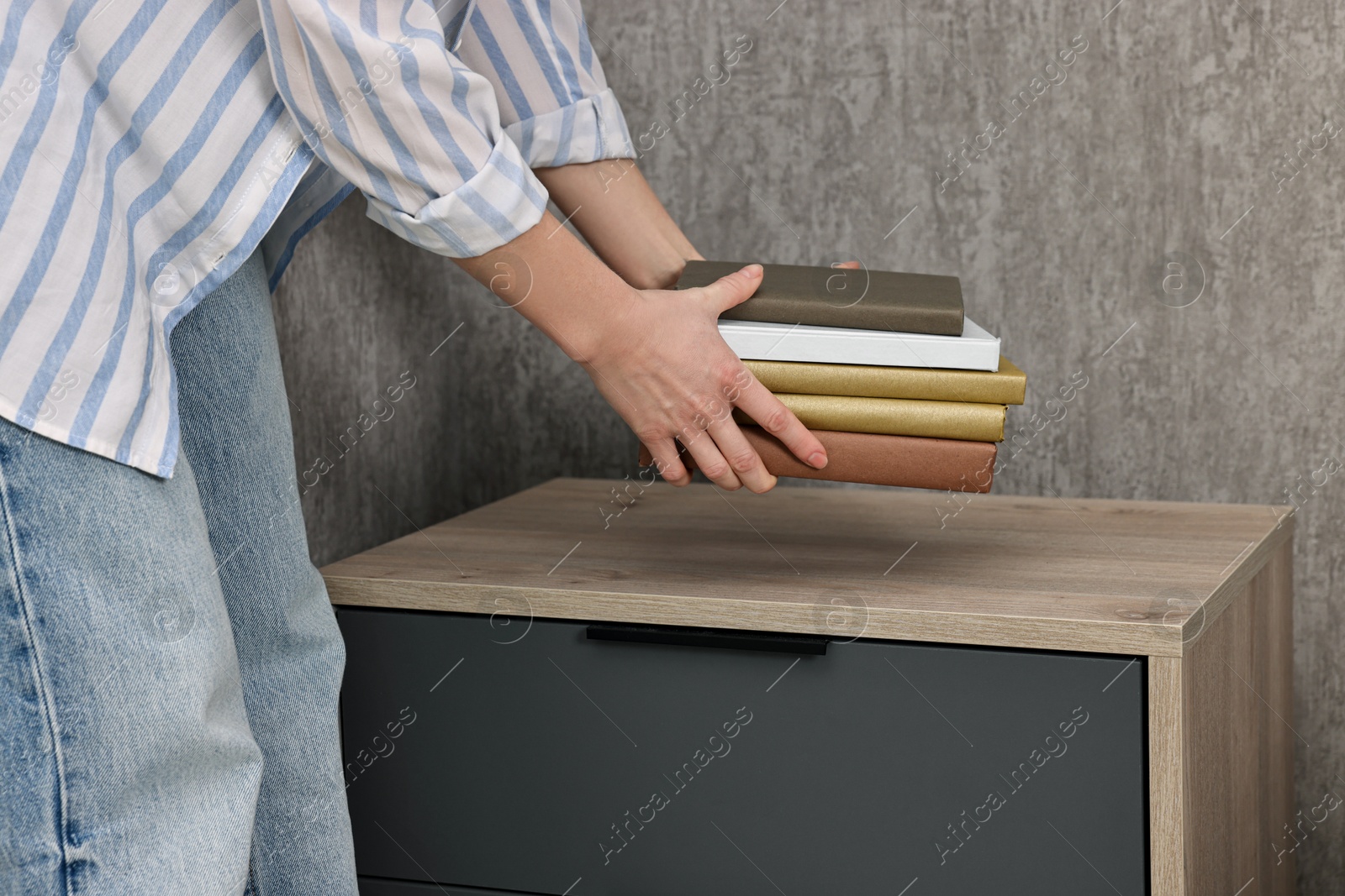 Photo of Female decorator arranging books onto nightstand indoors, closeup